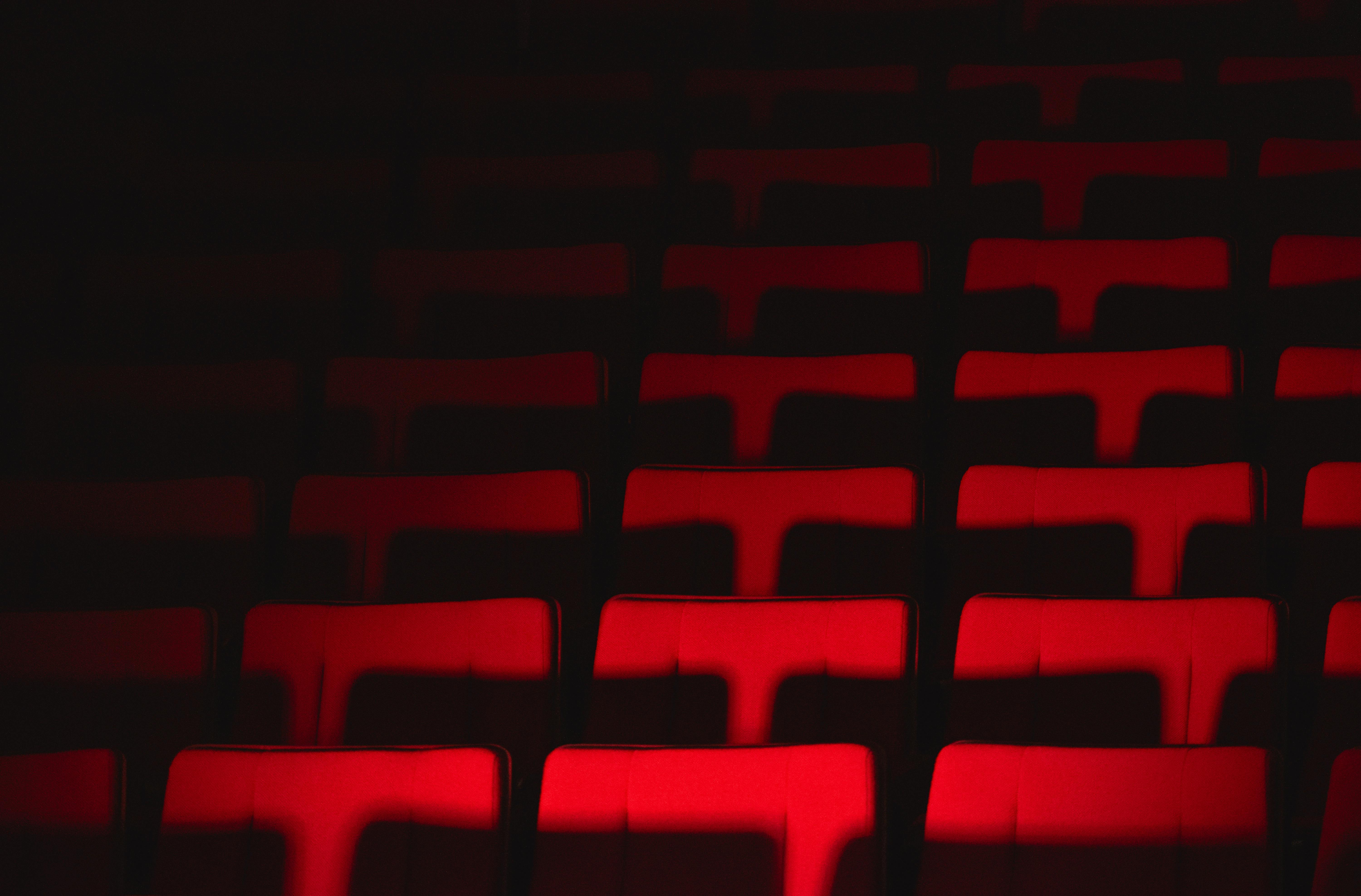 grátis Fileiras de assentos vazios no teatro, iluminadas dramaticamente, criam uma atmosfera melancólica. Foto profissional