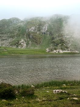 Serene view of misty mountains and lake in Covadonga, Spain, capturing natural beauty.