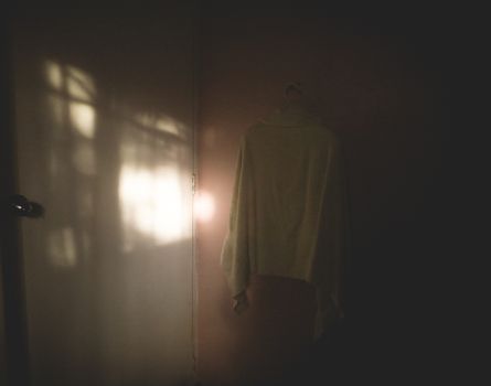 A minimalist interior space with soft morning light casting shadows on a wall and a sweater hanging in a calm setting.