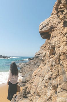 A woman enjoys the rocky shoreline of a serene beach on a sunny day.