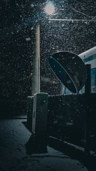 A captivating nighttime urban scene showcasing a snowy atmosphere with a vintage phone booth under streetlights.