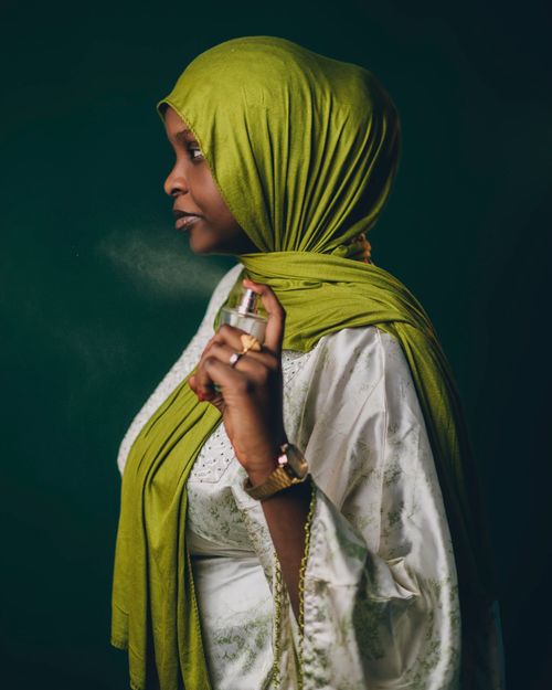 Free Portrait of a woman in a green hijab applying perfume, showcasing cultural elegance. Stock Photo