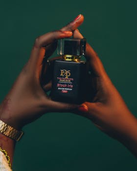 Close-up of hands holding black perfume bottle on green background. Elegant and stylish.
