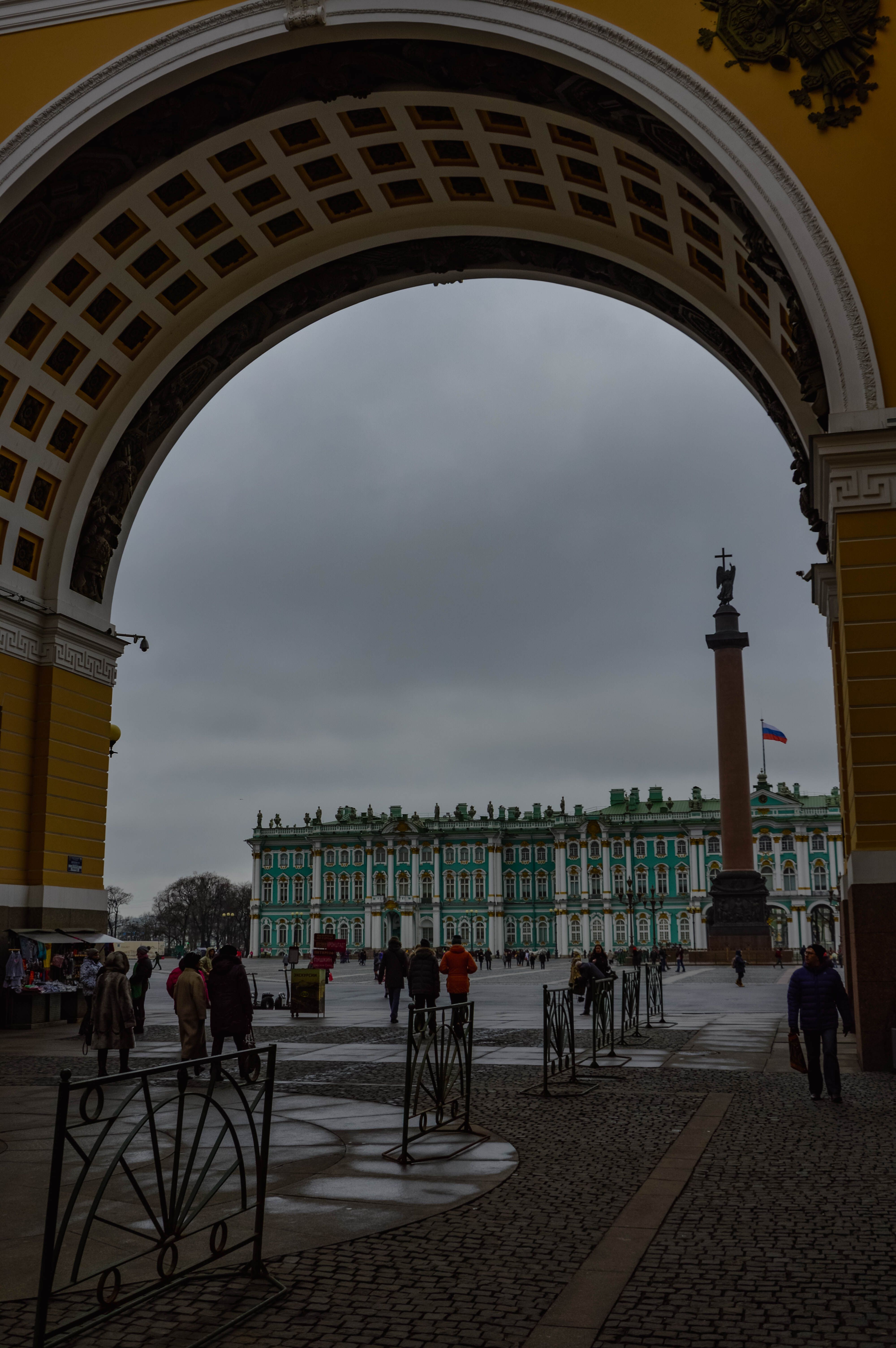 View of the Hermitage Museum in St. Petersburg framed by a historical archway, capturing a cloudy day.