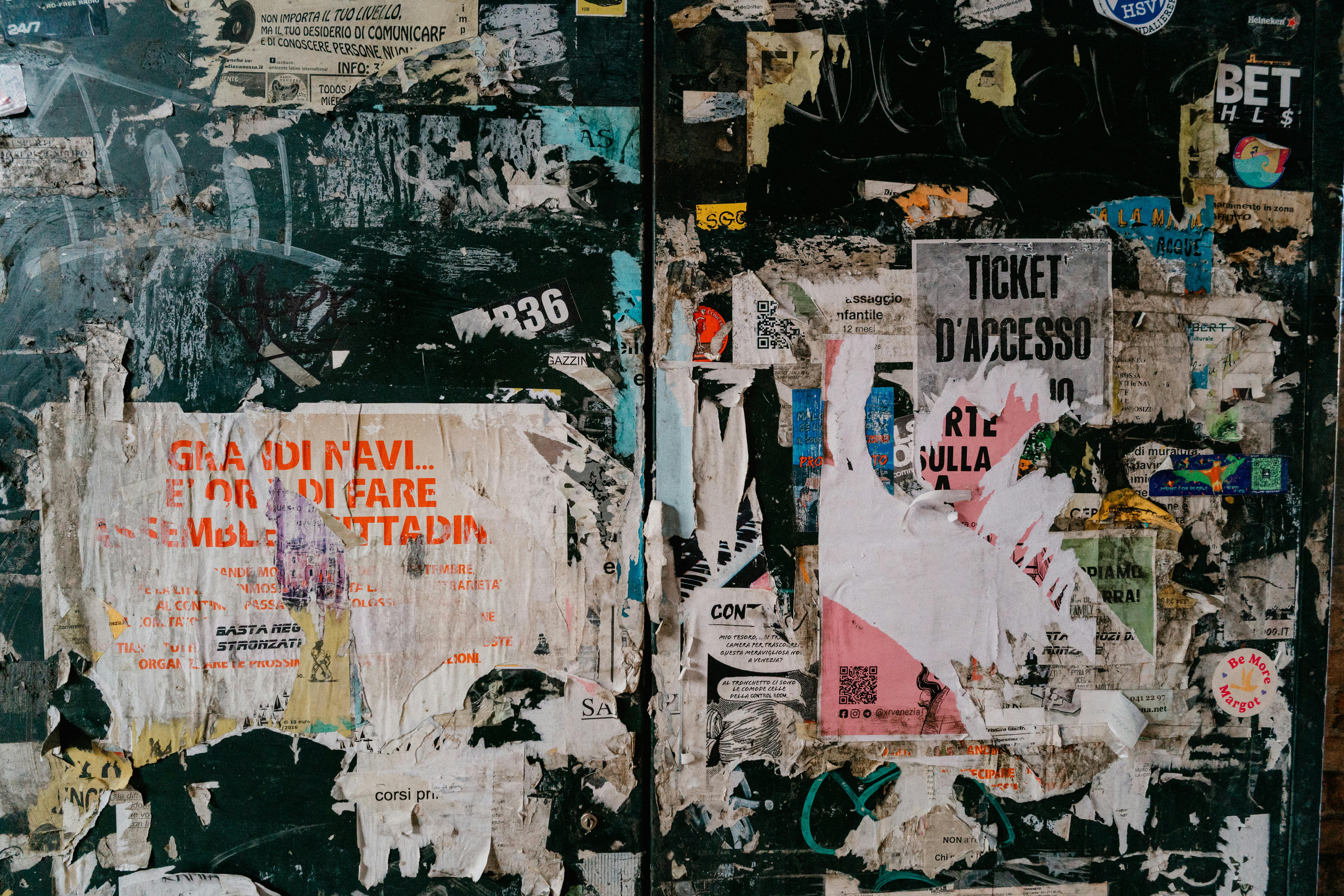 Gratis Un collage rustico di poster scrostati su un muro urbano usurato dal tempo, che crea un motivo strutturato vibrante. Foto a disposizione