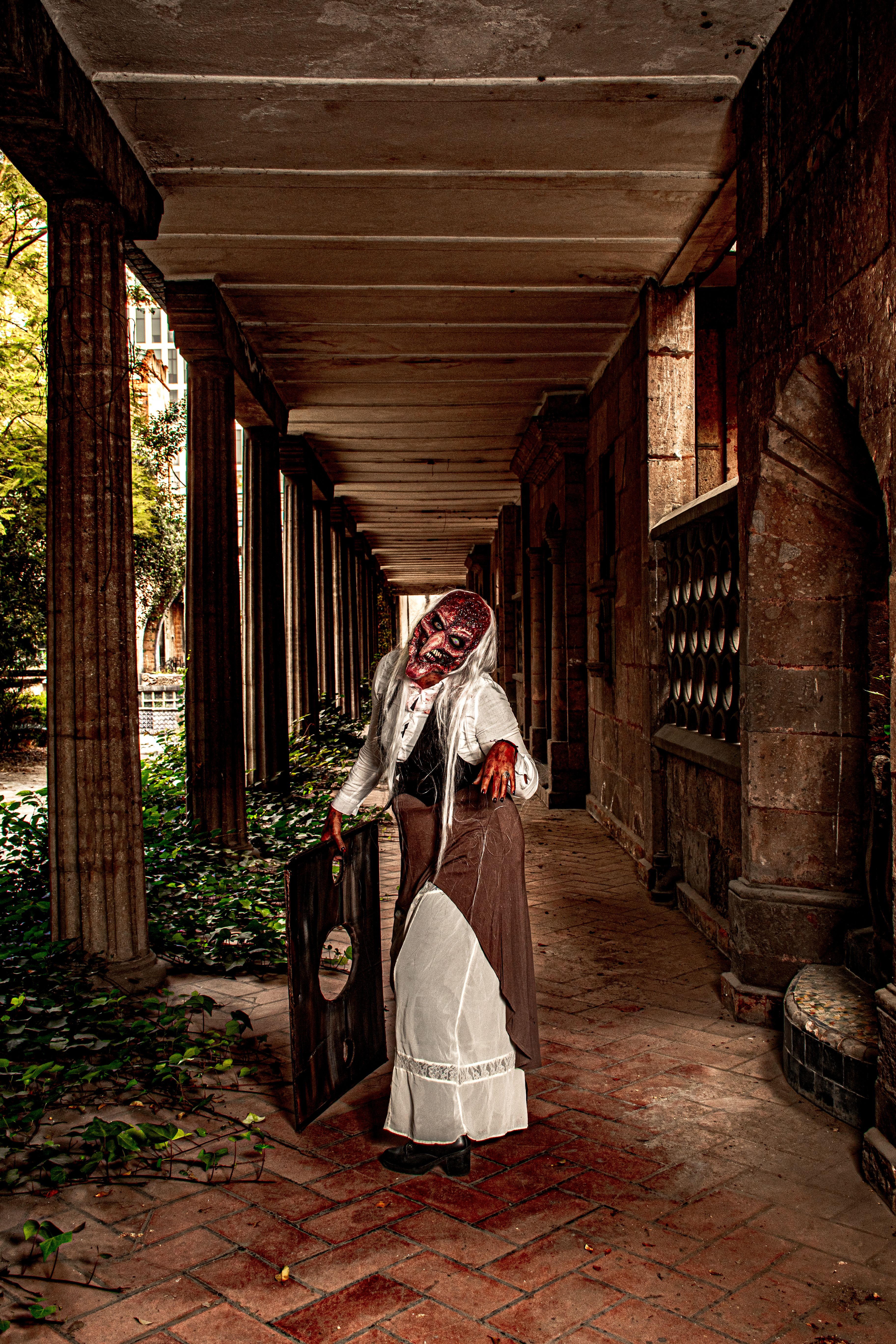 Eerie image of a zombie in a dilapidated corridor with overgrown foliage.