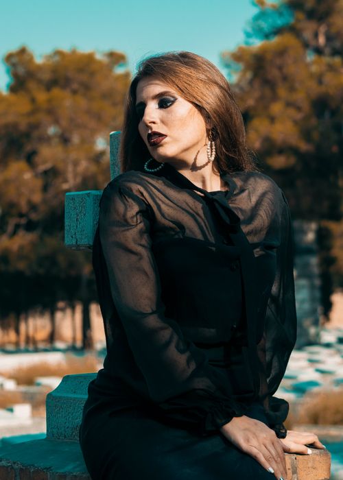 Free Thoughtful woman dressed in black clothes sitting on concrete headstone while grieving about death in cemetery Stock Photo