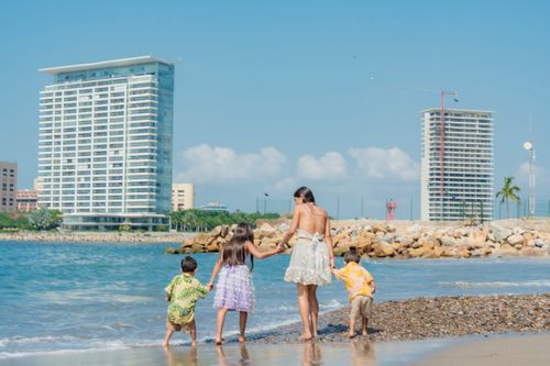 Free A happy family playing on a sandy beach with modern buildings in the background on a sunny summer day. Stock Photo