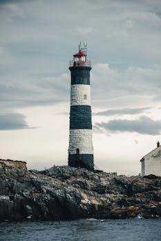 Dramatic view of a lighthouse on a rocky coast under a moody sky, perfect for travel and navigation themes.