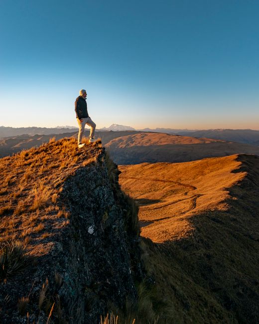 A lone hiker stands on a cliff's edge in Cusco, Peru, admiring the breathtaking Andean sunrise.