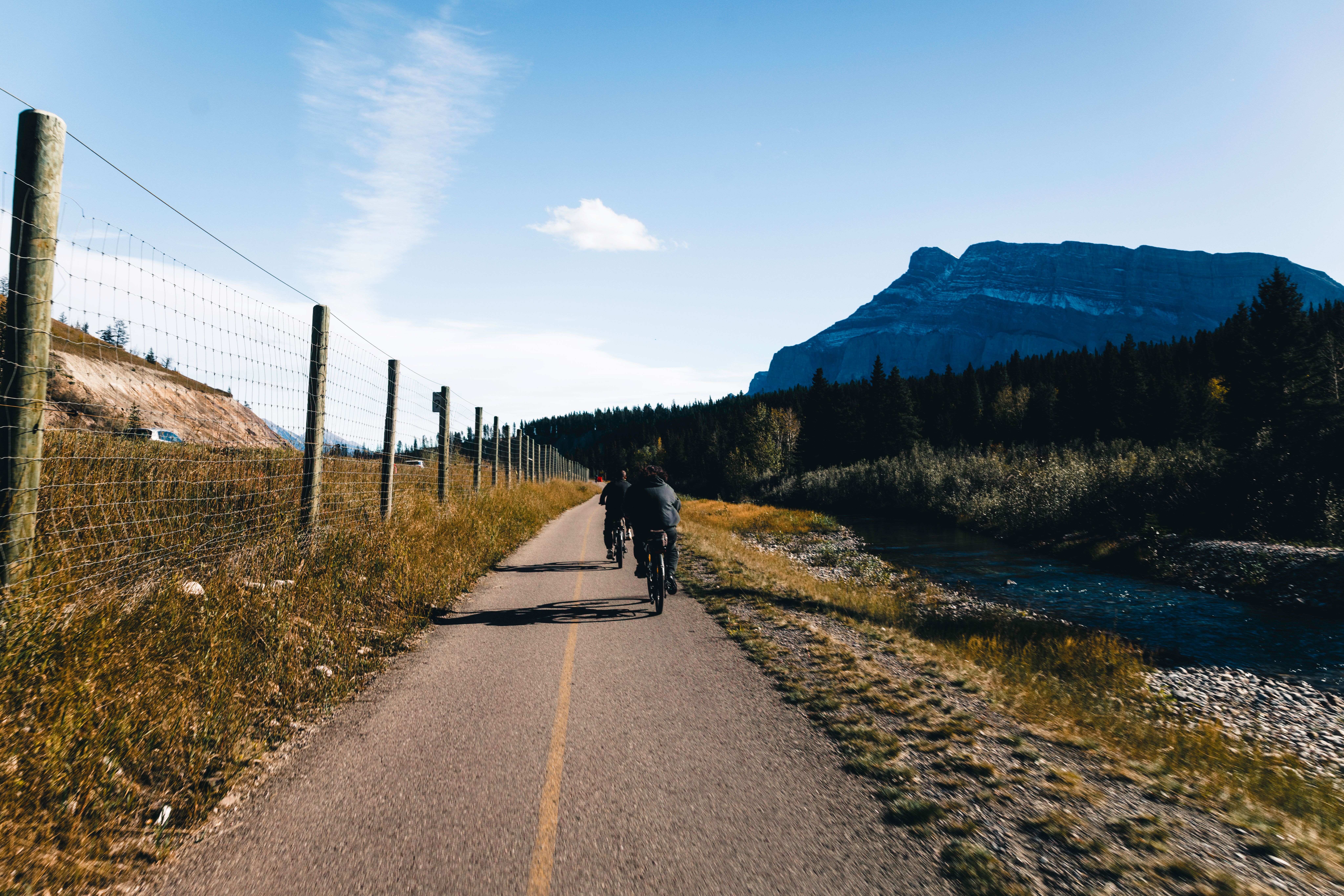Cyclists on a paved path through a forested river valley