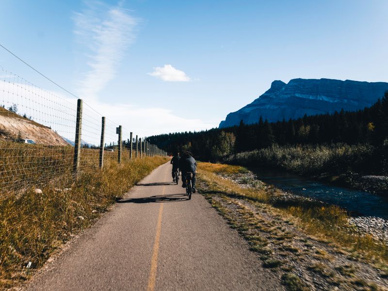 Cyclists on a paved path through a forested river valley