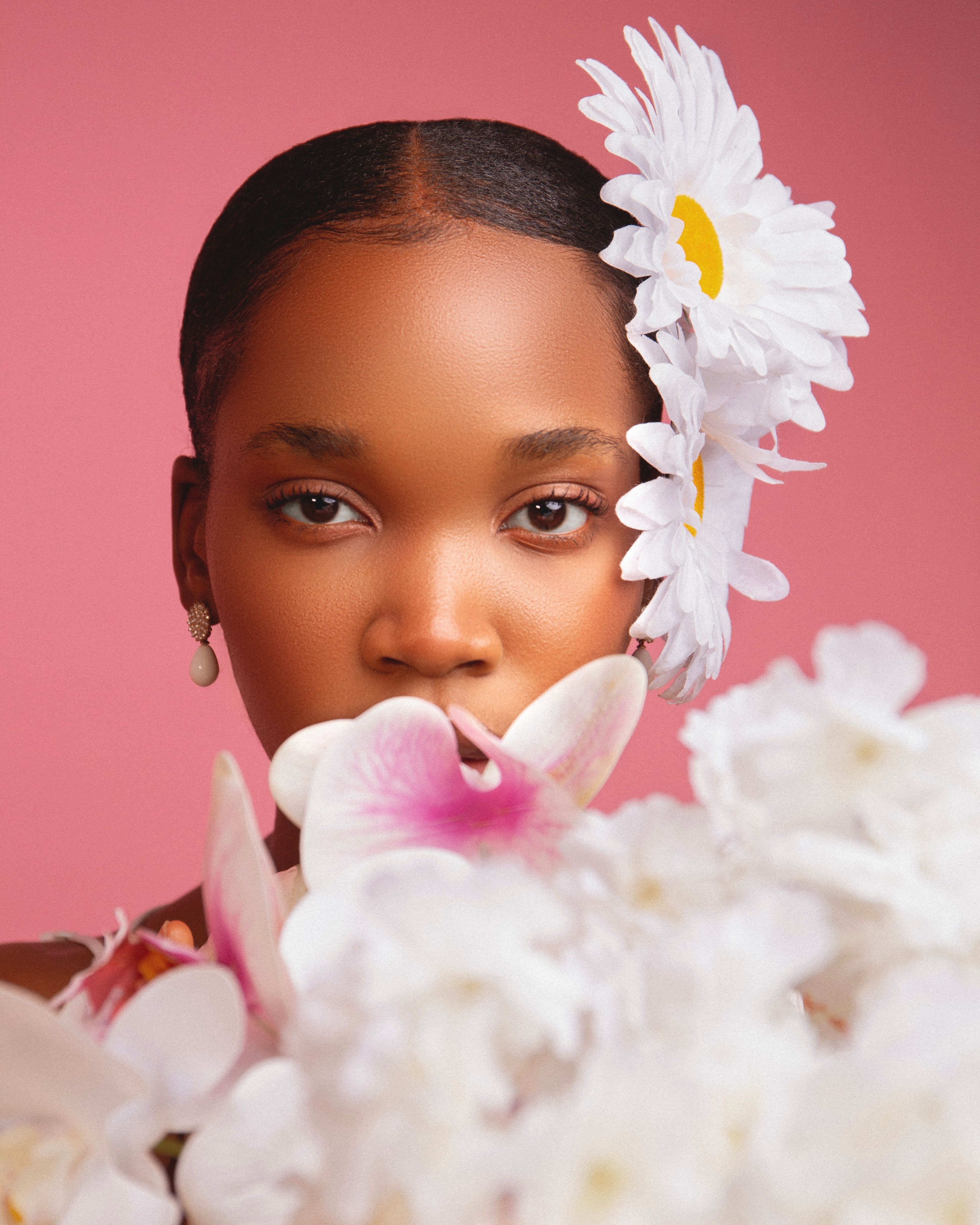 Beautiful portrait of a woman adorned with daisies and orchids set against a pink background.