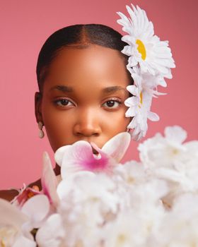 Beautiful portrait of a woman adorned with daisies and orchids set against a pink background.