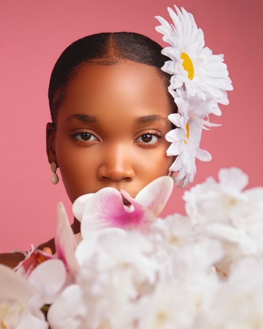 Beautiful portrait of a woman adorned with daisies and orchids set against a pink background.