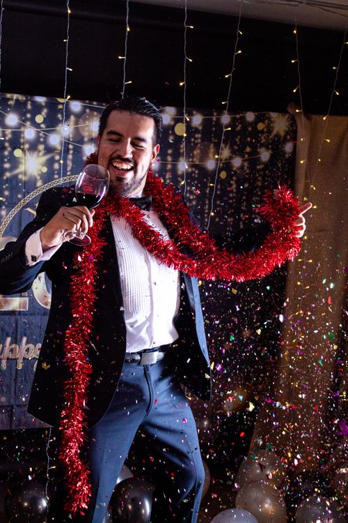 Free Joyful man celebrating New Year's with confetti and wine indoors. Stock Photo