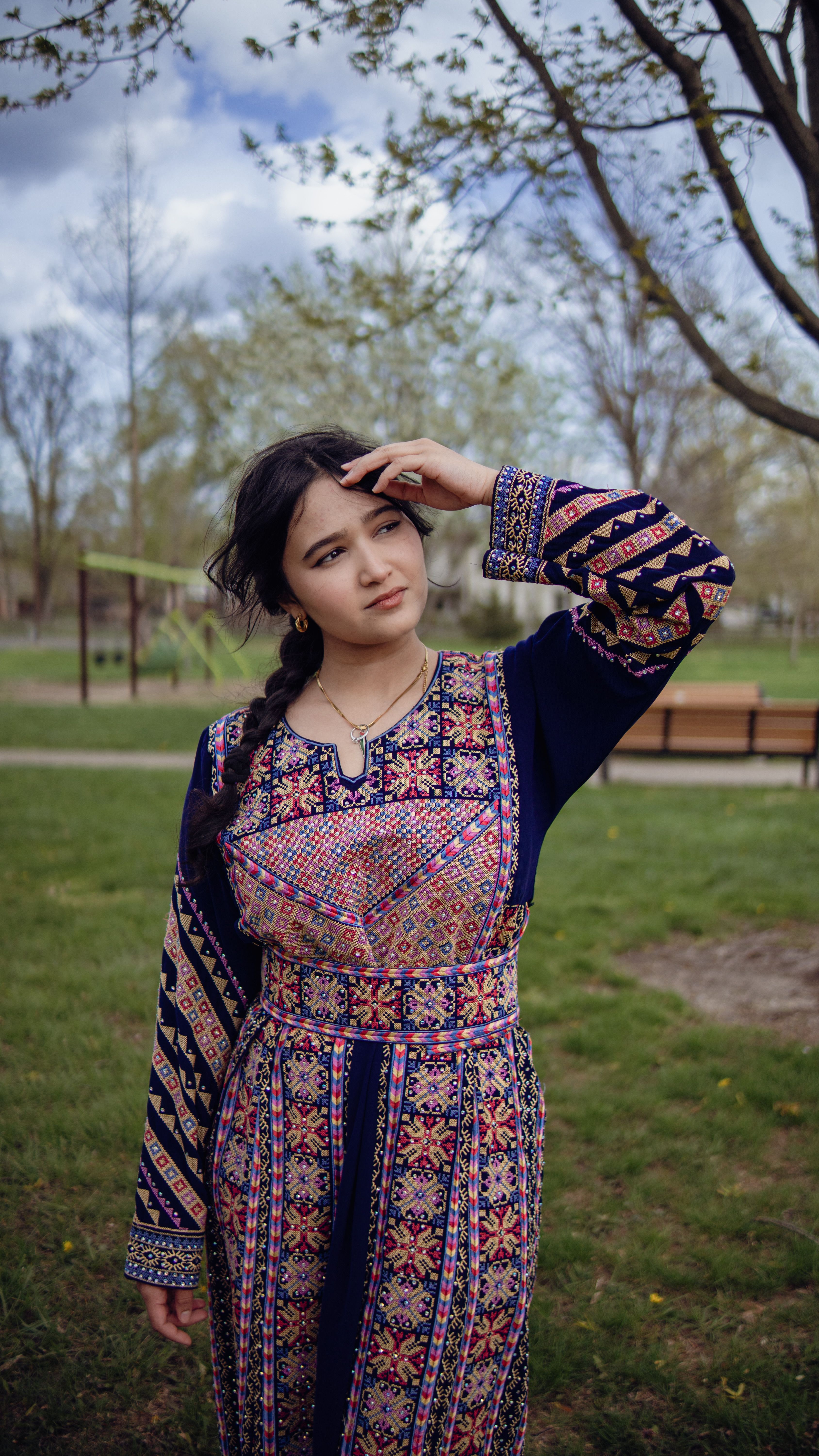 Woman posing in colorful traditional embroidered dress in a park setting during daytime.