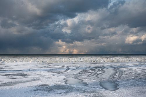 Free A breathtaking view of a frozen seashore under dramatic, cloudy skies, captured in winter. Stock Photo