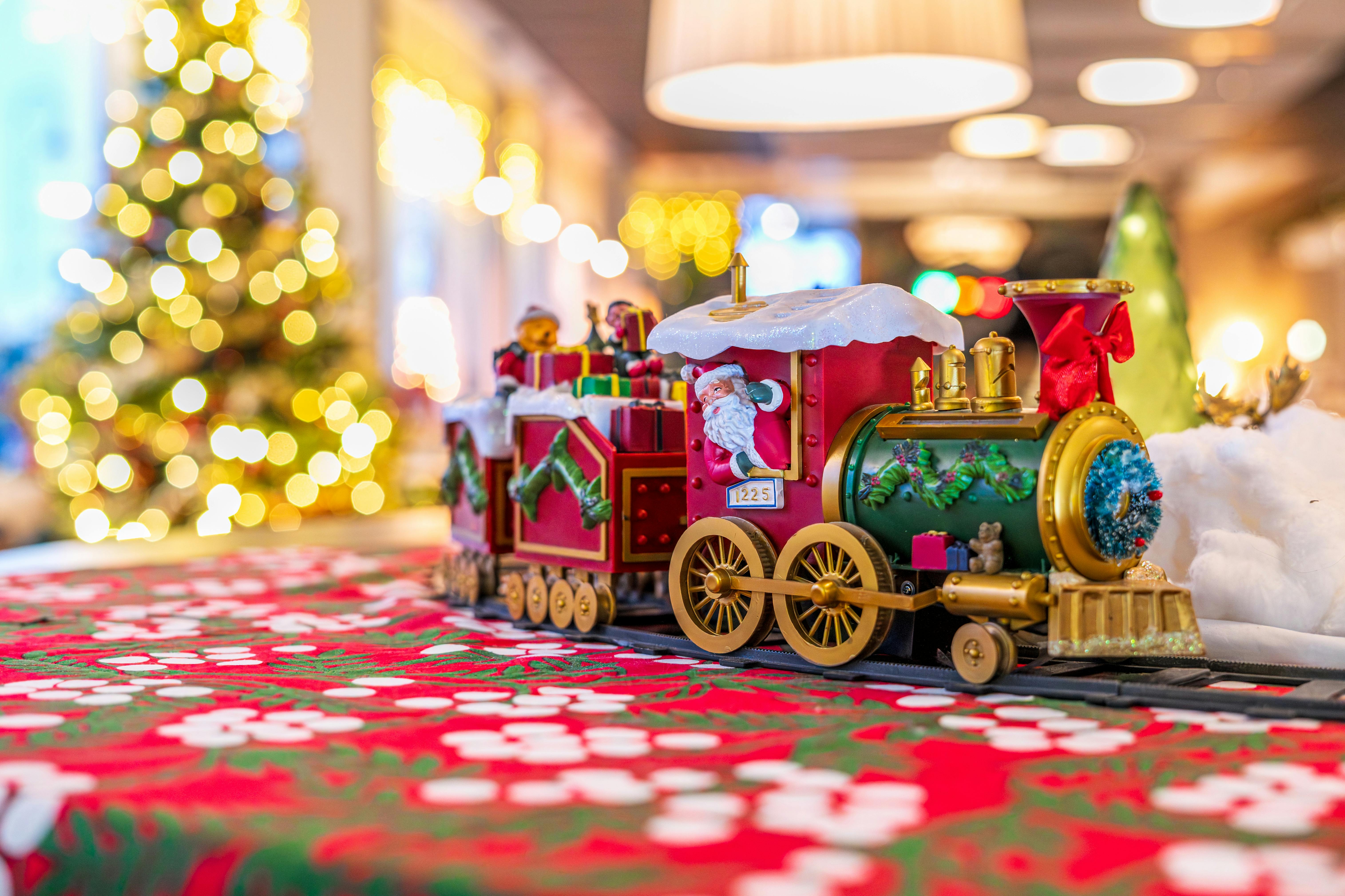 Colorful toy train with Santa, surrounded by holiday lights and decor, evokes festive Christmas spirit.
