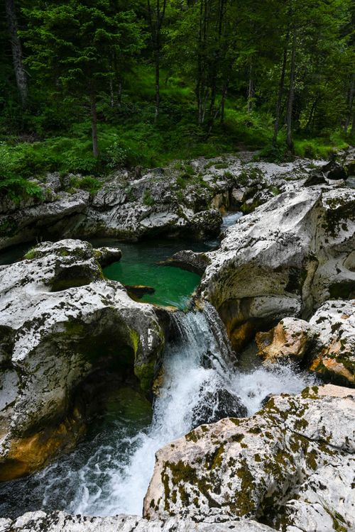 Free Serene mountain stream cascading into an emerald pool surrounded by lush greenery and rugged rocks. Stock Photo