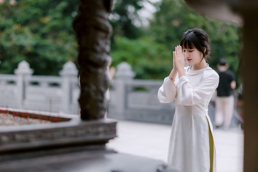 Young woman in a traditional dress offering prayers outdoors in a serene setting.