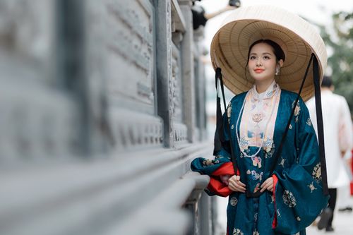 Free Elegant woman in traditional Asian robe with a conical hat standing by a wall outdoors. Stock Photo