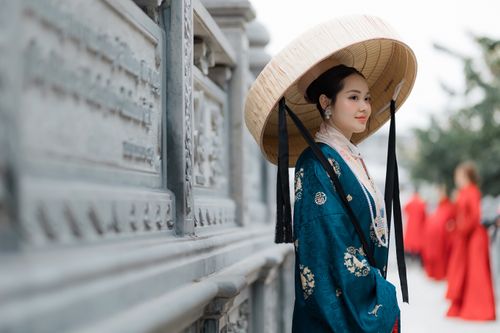 Free Woman in traditional Asian outfit and straw hat near ornate wall, cultural setting. Stock Photo