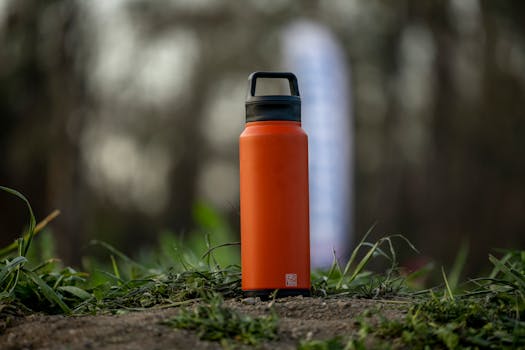 A vibrant orange water bottle sits on grass in an outdoor setting, perfect for hiking and adventures.