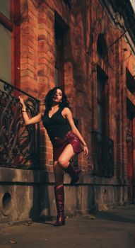 Stylish woman in red outfit leans against a decorative iron fence, showcasing urban fashion.