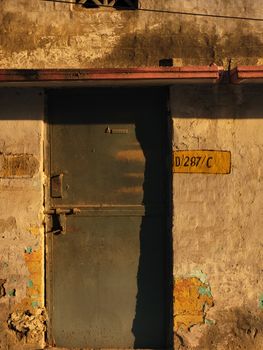 An old metal door on a distressed wall illuminated by golden hour light.
