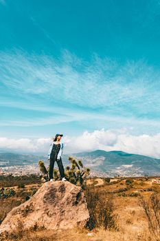 Woman standing on rock with mountains in background under clear sky.