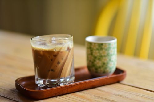 Free A glass of iced coffee and floral cup on a wooden tray in a cozy setting. Stock Photo