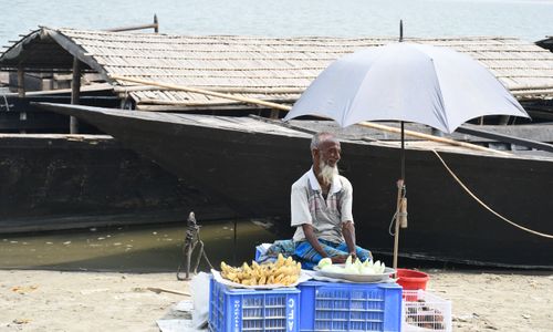 Free An elderly vendor sells fruits by a river in Rangpur, Bangladesh, under a parasol. Stock Photo