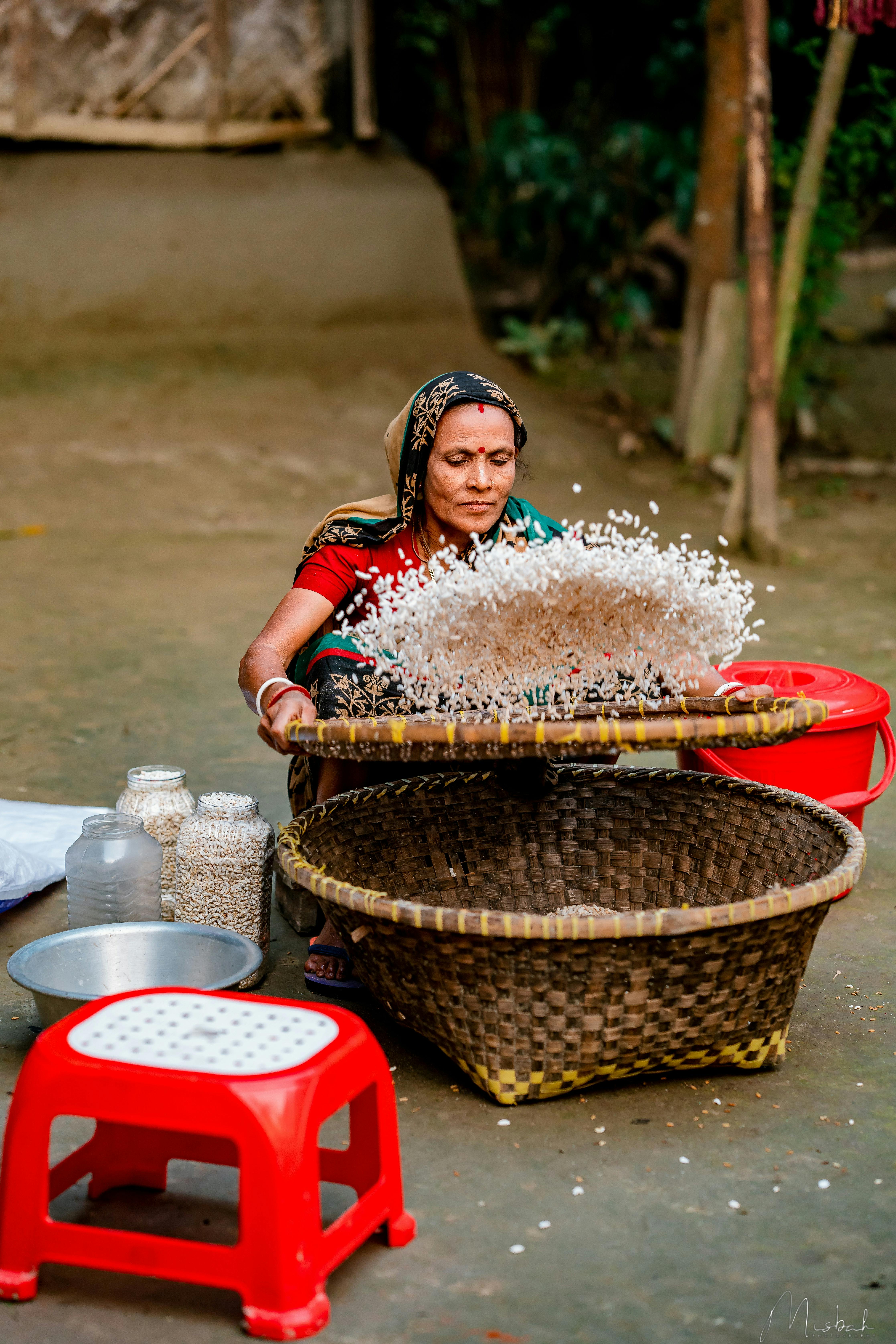 Gratis En kvinne som sikter ris med tradisjonelle verktøy i et utendørs landlig miljø. Arkivbilde