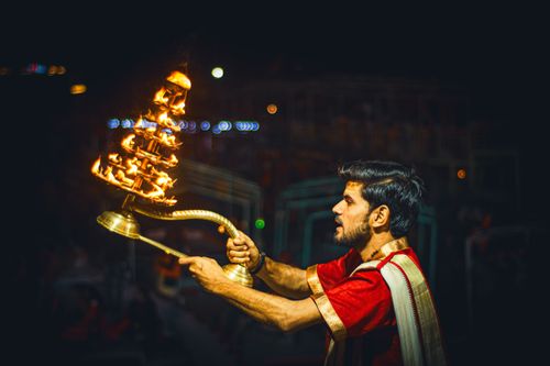 Free A man in traditional attire performing a Hindu ritual with a large fire lamp during nighttime. Stock Photo