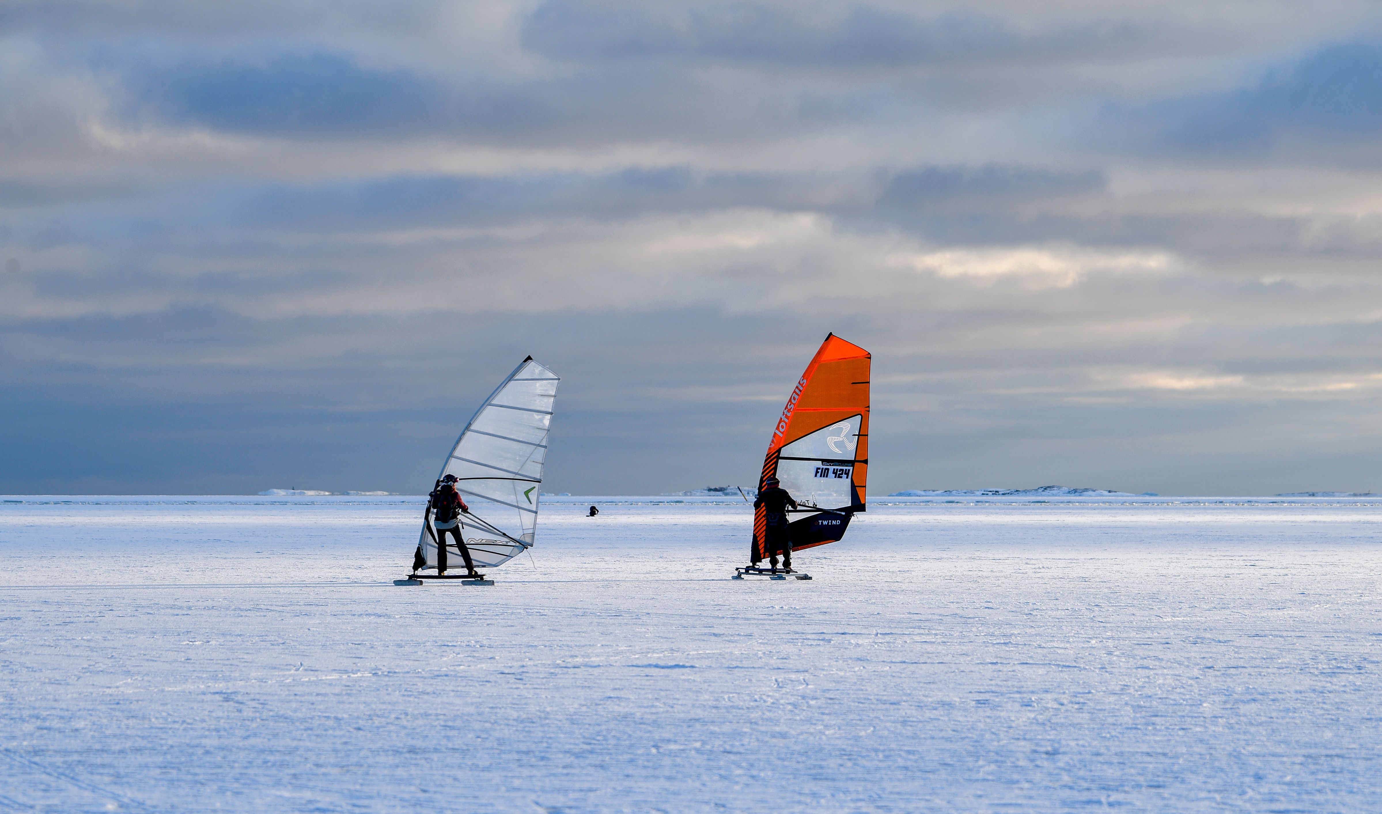 Two people ice sailing on a frozen sea in Helsinki, capturing a unique winter sport under a clear sky.
