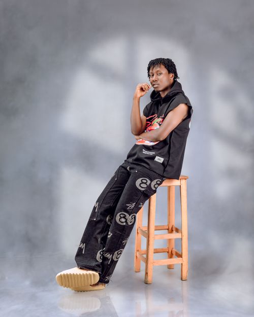 Free Young adult in casual wear striking a pose on a wooden stool against a gray background. Stock Photo