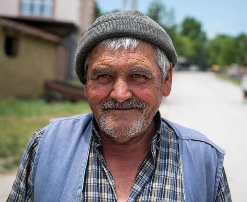 Free Close-up portrait of a smiling elderly man wearing a beanie, outdoors on a sunny day. Stock Photo