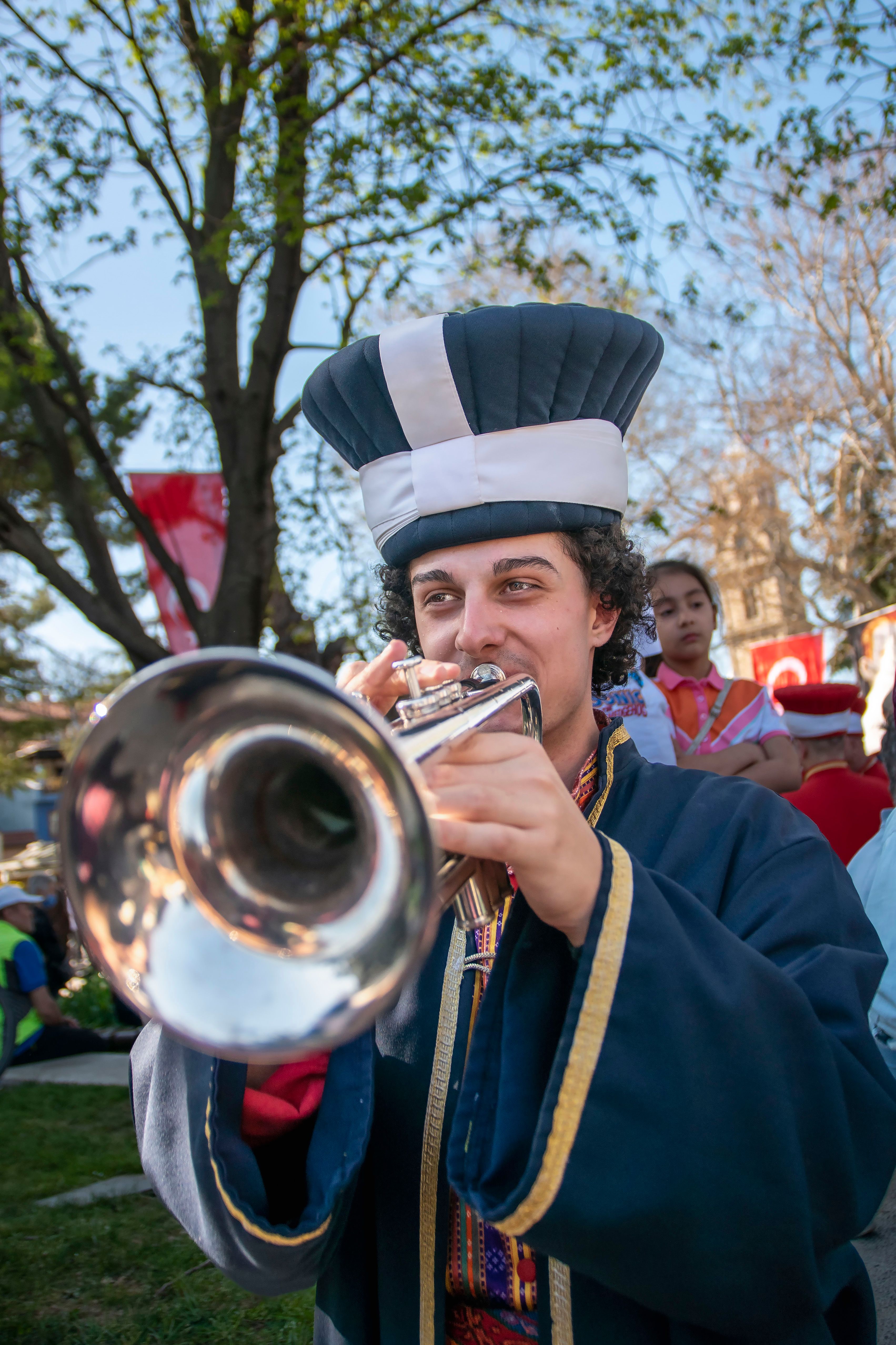 Musician in traditional costume plays trumpet during outdoor festival, creating a lively atmosphere.