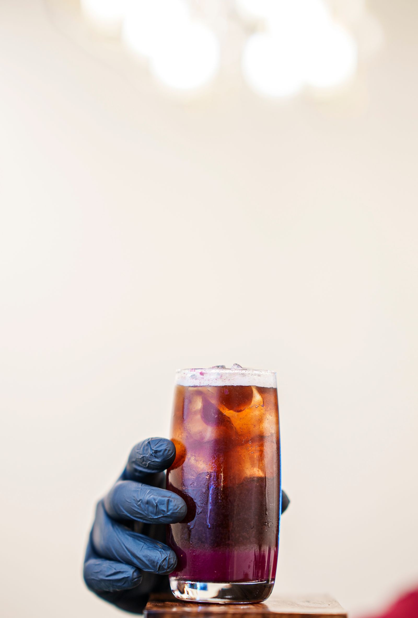 A close up of a layered purple iced drink in a clear glass held by a gloved hand