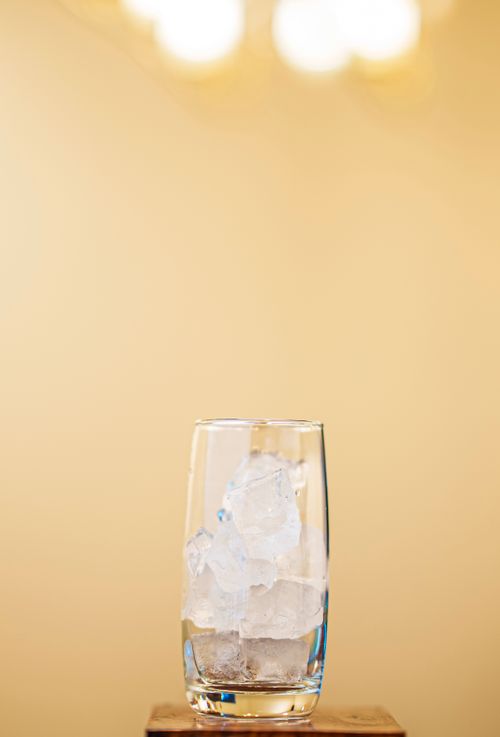 Free Close-up of a clear glass filled with ice cubes placed on a wooden surface against a warm background. Stock Photo