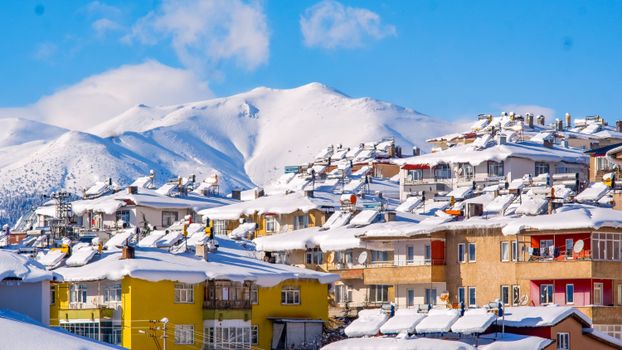 Vibrant village houses topped with snow set against majestic snowy mountains.
