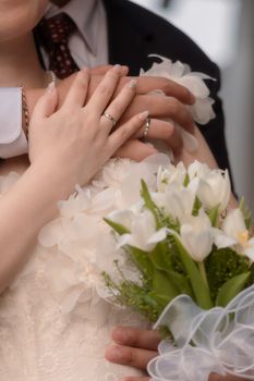 Close-up of a newlywed couple embracing, showcasing wedding rings and a floral bouquet.