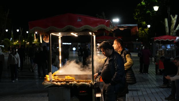 Night market scene with a vendor selling steaming corn on the cob.