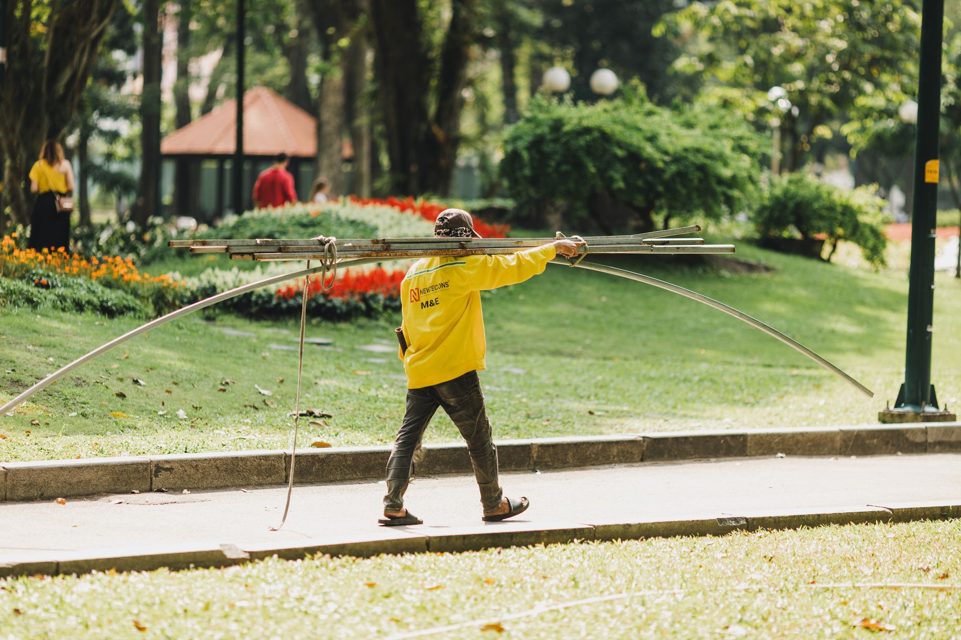 A worker carrying metal pipes in a lush park in Ho Chi Minh City, Vietnam.