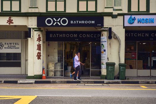 Man walking past storefronts in colorful Singapore street, featuring OXO Bathroom.