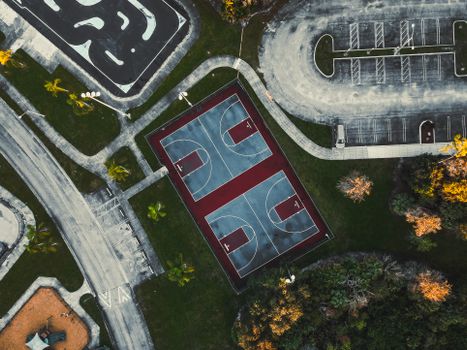 An aerial shot of an empty basketball court in a public park, featuring geometric design and suburban surroundings.