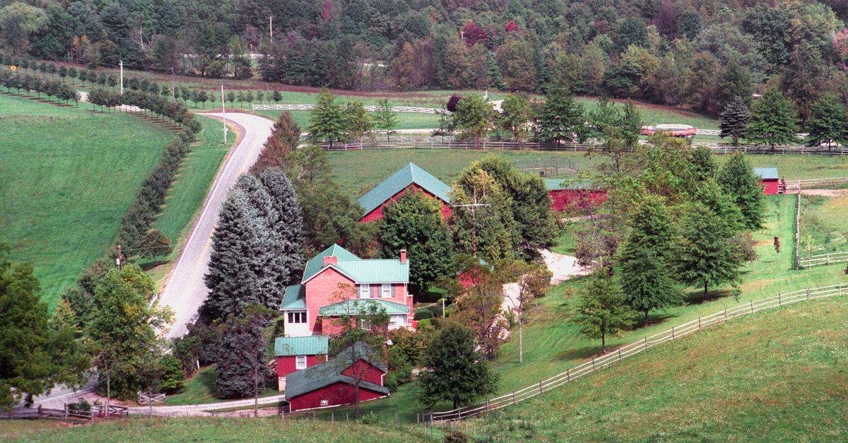 Picturesque farm scene with red barn, lush trees, and winding road.