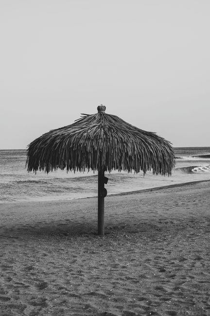 Black and white photo of a straw umbrella on a deserted tropical beach, capturing tranquility and simplicity.
