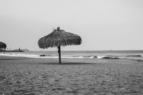 Free A serene black and white photo of a beach with a solitary straw umbrella, capturing peaceful coastal vibes. Stock Photo